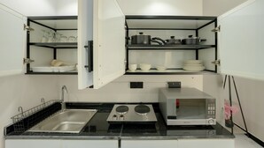 A compact kitchen with a built-in sink, two stovetops, a microwave, and open shelving with dishes and cookware.