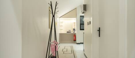 A hallway with a black coat rack, a potted plant, and a rug leading to a kitchen area with a sink and a fire extinguisher.