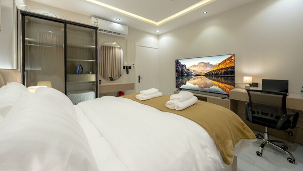 A hotel room with a bed, a desk with a computer, a TV, and a wardrobe.