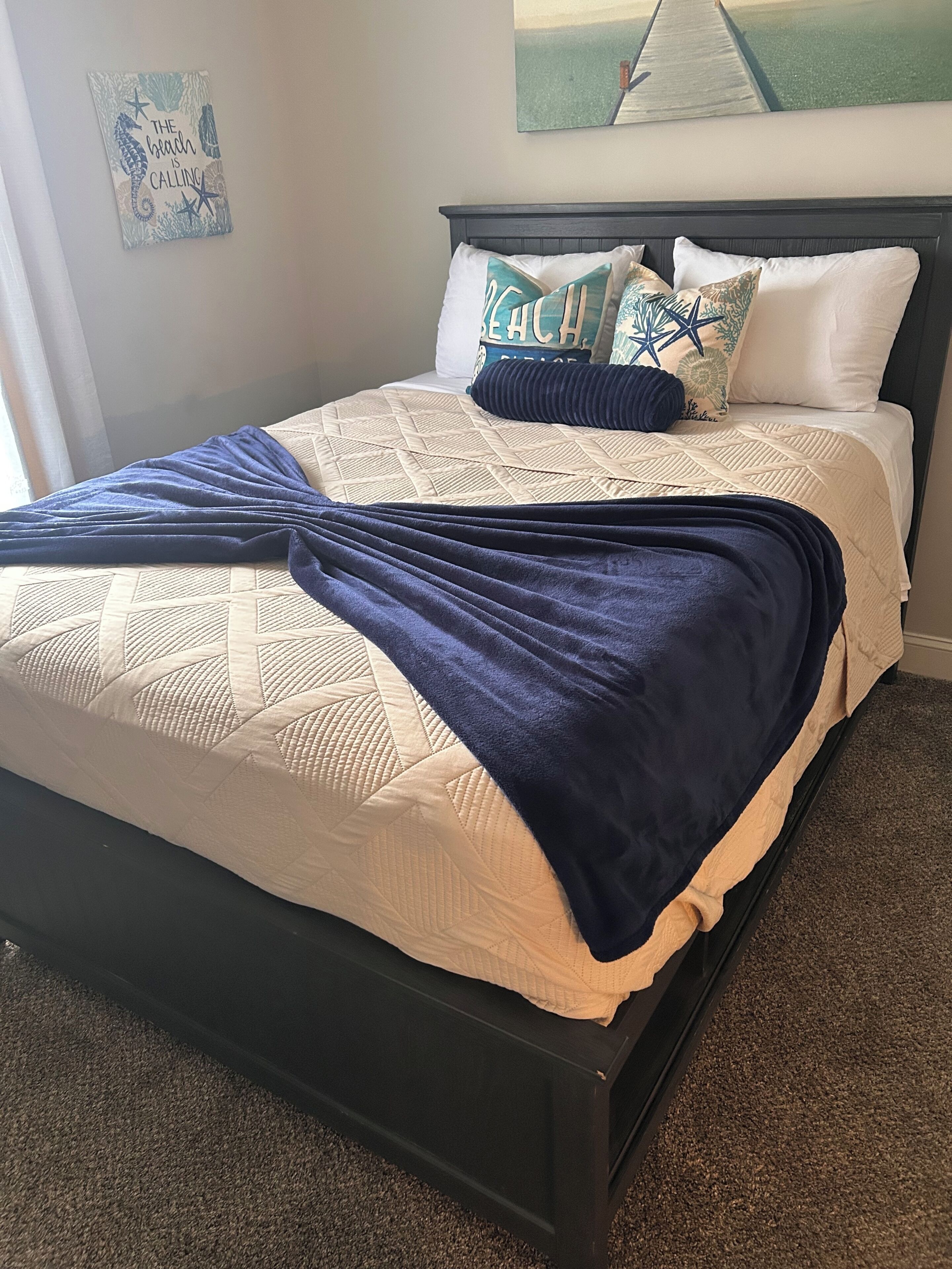 A bed with a quilted headboard, a navy blue blanket, and decorative pillows.
