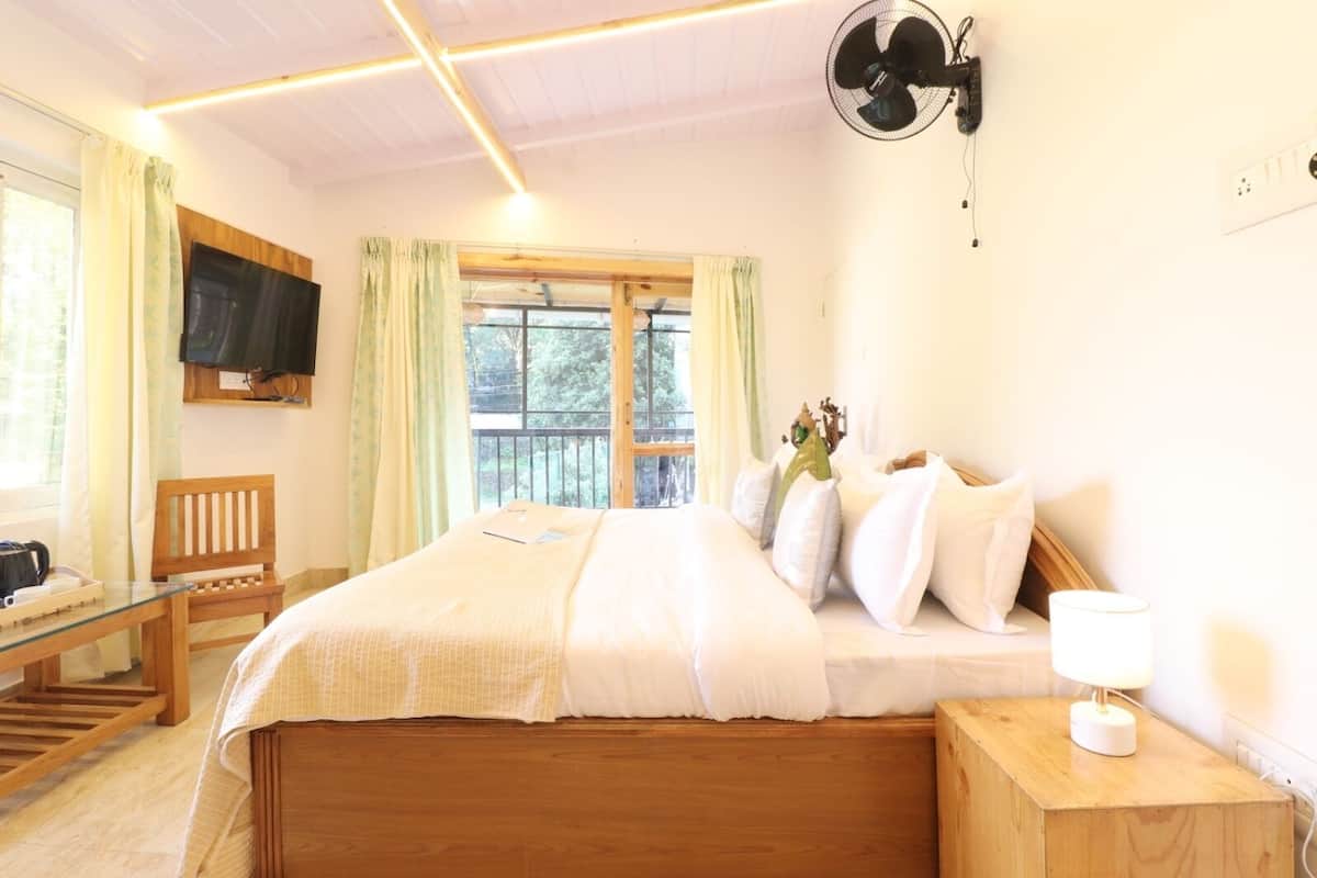 A bedroom with a wooden bed, a bedside table with a lamp, a chair, a TV mounted on the wall, and a window with curtains.