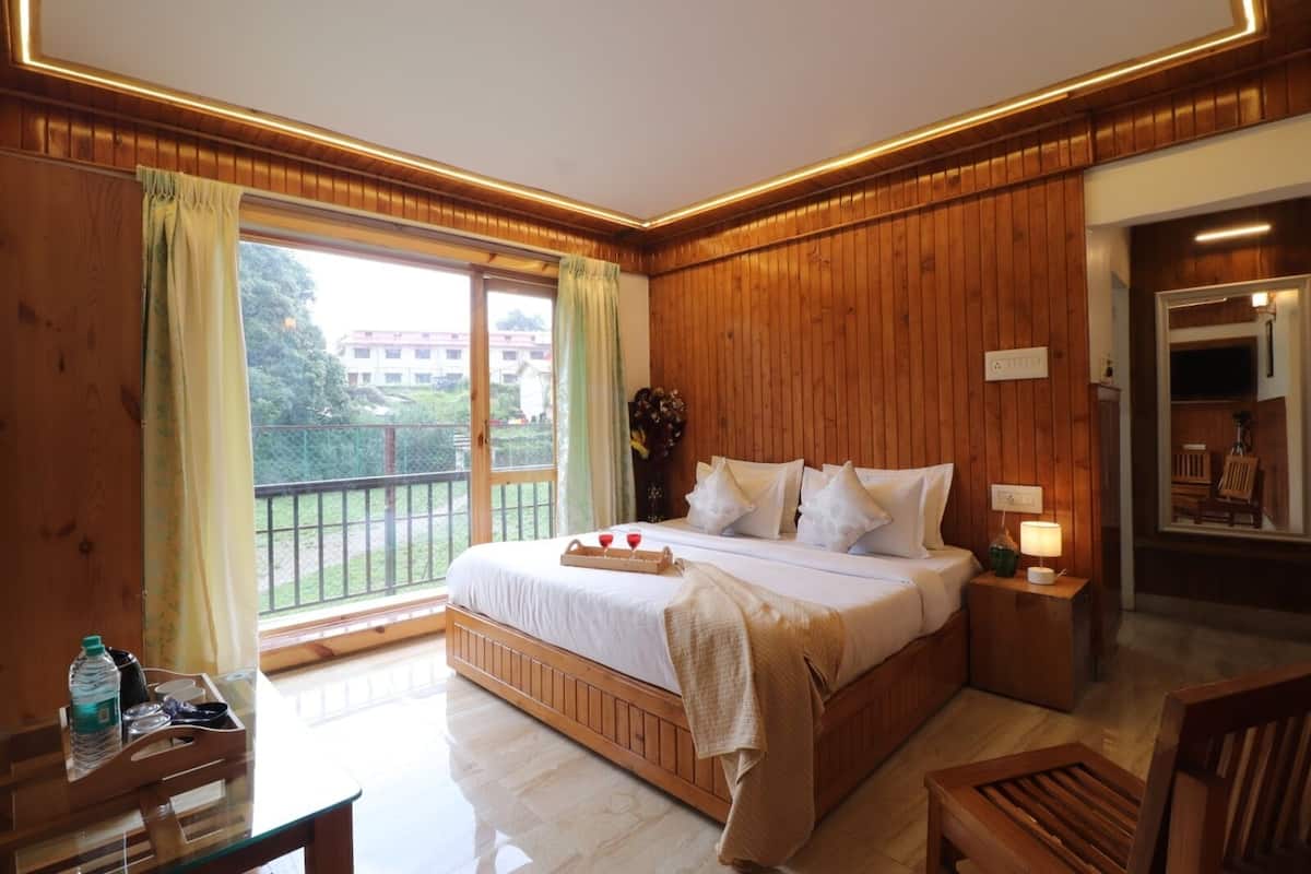 A wooden-paneled bedroom with a large bed, a bedside table with a lamp, a window with curtains, and a view of the outside.