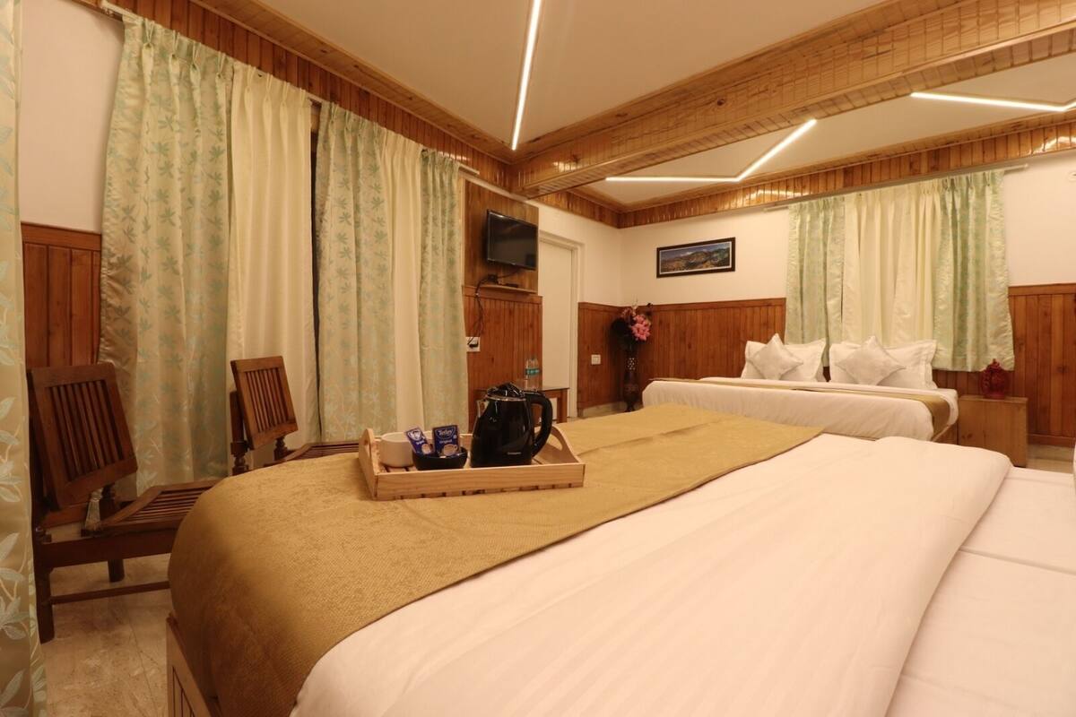 A hotel room with two beds, wooden paneling, a flat-screen TV, and a tray with breakfast items.