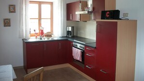 Una cocina compacta con armarios rojos, horno integrado y microondas.