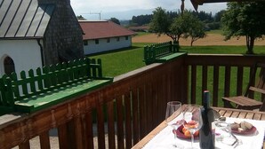 Una terraza de madera con una mesa lista para comer, con vistas a un paisaje rural que incluye una iglesia y campos.