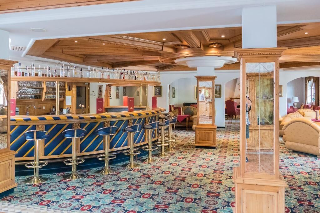 Eine Bar mit einer gebogenen Theke, mehreren Hockstühlen und einem gemusterten Teppich.