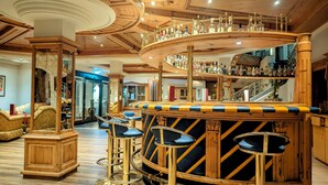A bar area with a curved wooden counter, multiple stools, and a variety of bottles. - Parkschlössl zu Thyrnau (Thyrnau)