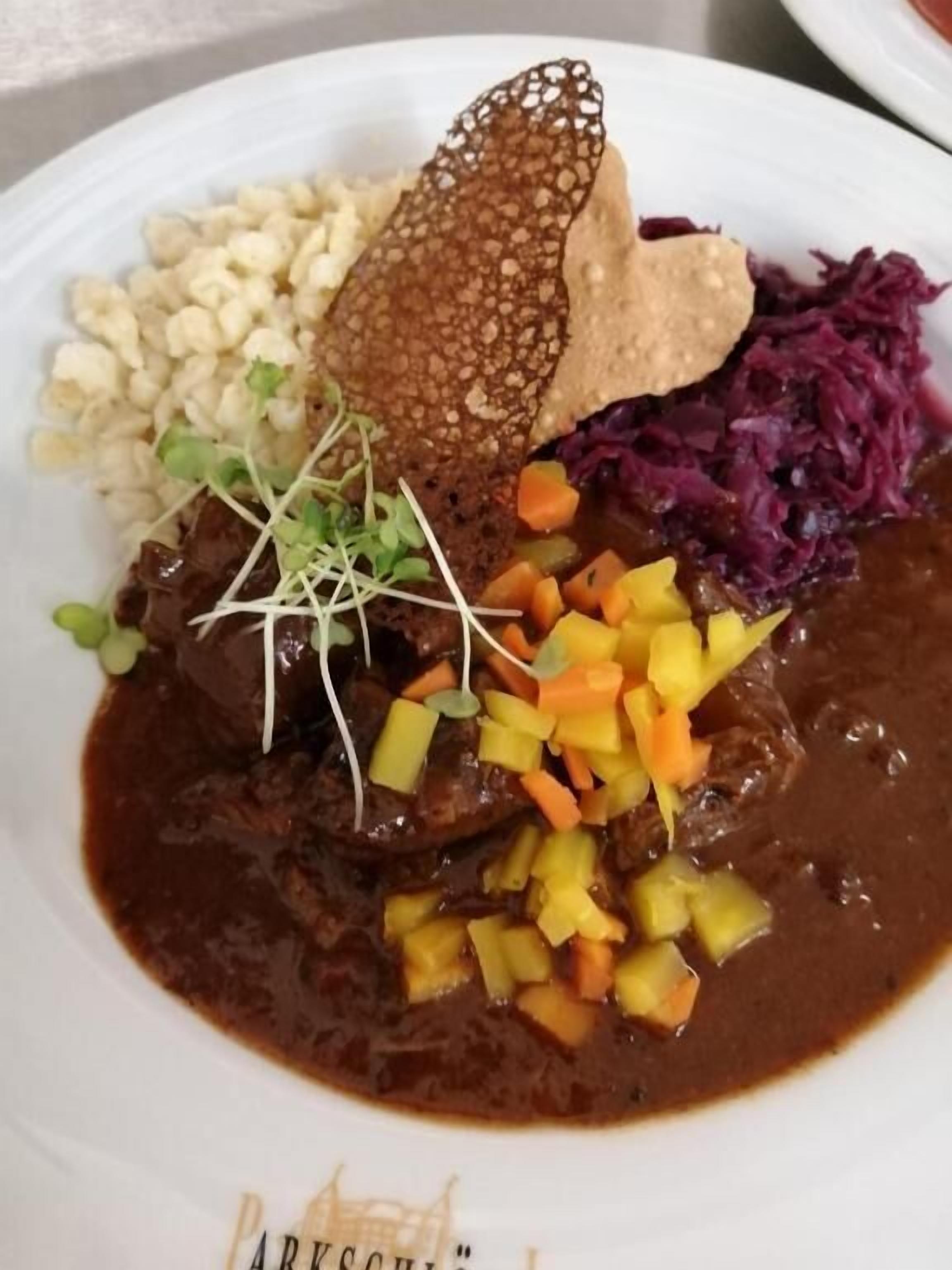 Un plato de comida con diversos elementos, incluyendo un guiso de carne con verduras y una rebanada de pan.