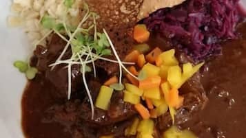 Un plato de comida con diversos elementos, incluyendo un guiso de carne con verduras y una rebanada de pan.