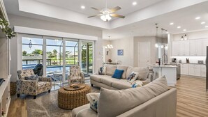 A spacious living area with a large window, a ceiling fan, and a kitchen area with white cabinets.