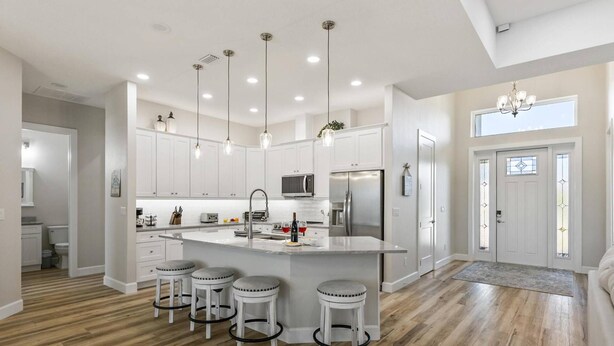 A modern kitchen with white cabinets, a central island with bar stools, stainless steel appliances, and pendant lighting.