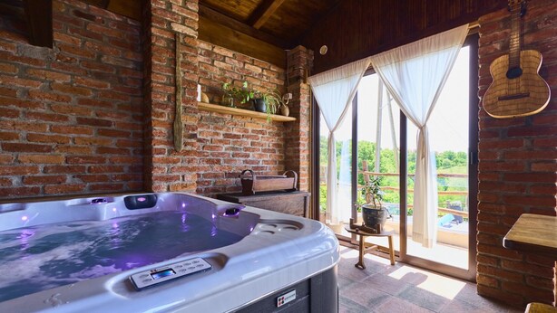 Un jacuzzi en una habitación rústica con paredes de ladrillo, techo de madera y vistas al exterior.