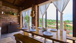 Una mesa de comedor de madera dispuesta con platos y cubiertos, una guitarra y vistas a la vegetación a través de amplios ventanales.