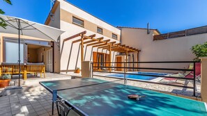 Una mesa de billar con una paleta de tenis de mesa, un banco de madera y una estructura de pérgola en un entorno residencial.