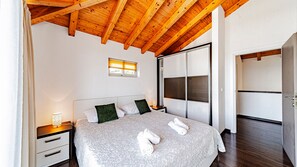 Un dormitorio con techo de madera, una cama con almohadas, una mesita de noche con lámpara y un armario con puerta corredera.