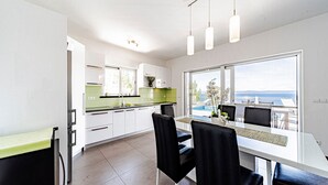 A modern kitchen with white cabinets, a green backsplash, and a dining area with a view of the sea. - Villa Antonia by Villas Guide (Smokvica)