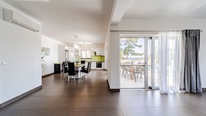A spacious living area with a dining table, chairs, a kitchen in the background, and a sliding glass door leading to an outdoor patio. - Villa Antonia by Villas Guide (Smokvica)