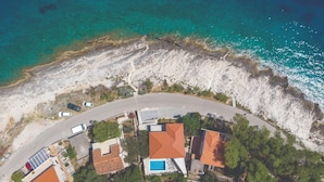 Vista aérea de una propiedad costera con un camino curvo, varios edificios y una piscina.