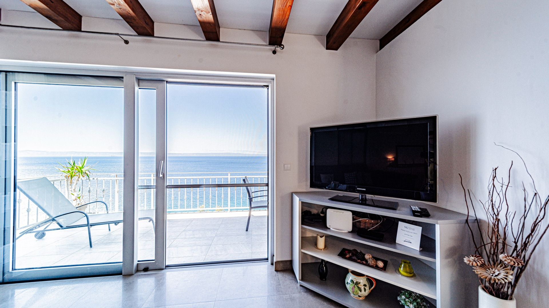 A living room with a large sliding glass door leading to a balcony with a view of the sea.