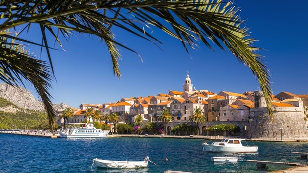 Un pueblo costero con edificios históricos, una torre destacada y barcos amarrados en el puerto deportivo.
