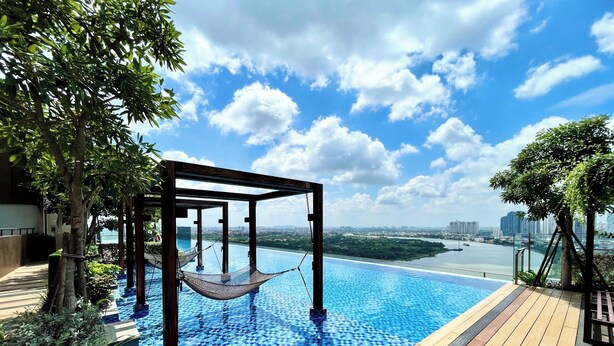 Piscina infinita en la azotea con una hamaca, terraza de madera y vistas a un río y al horizonte de la ciudad.