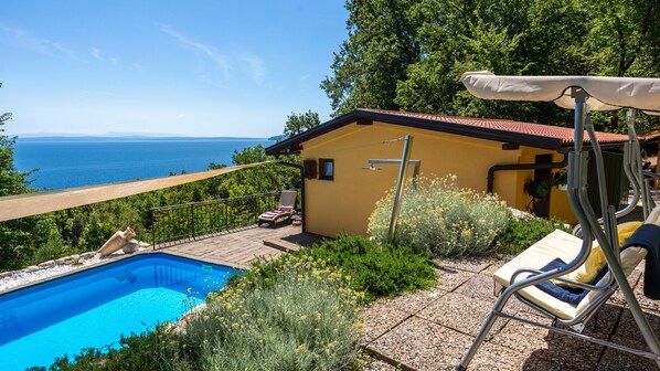 Ein Poolbereich mit Blick auf das Meer, ein gelbes Gebäude und eine überdachte Sitzgelegenheit.