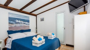 Ein Schlafzimmer mit einem Bett, einem Strandbild, einer Tür und einem Fernseher an der Wand.