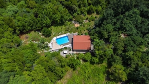 An aerial view of a property with a swimming pool and a red-roofed building surrounded by dense green forest.