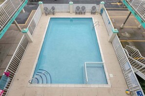 A rectangular pool with a diving board, surrounded by a white fence and chairs.