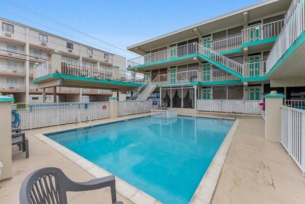 A swimming pool surrounded by a multi-story building with balconies and staircases.