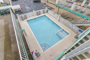 A rectangular pool with a diving board, surrounded by a white fence and chairs.