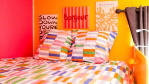 Sängyssä on värikkäät raidalliset vuodevaatteet, seinällä on «Bonjour»-kyltti ja Matisse-aiheinen taideteos.