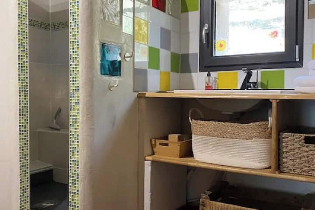 A bathroom with a tiled shower area, a sink with a mirror, and a shelf with baskets.