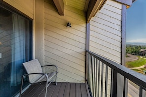 A balcony with a chair, a window, and a view of a road and greenery.