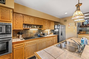 A kitchen with wooden cabinets, a stainless steel sink, a microwave, a stove, and a refrigerator.