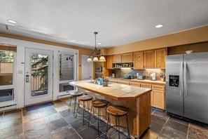 A modern kitchen with a central island, bar stools, wooden cabinets, and stainless steel appliances. - Walk to Resort | Hot Tub | Great Views | 4enSuites (Steamboat Springs)