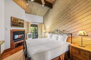 A bedroom with a bed, a fireplace, a television, and a window with curtains.