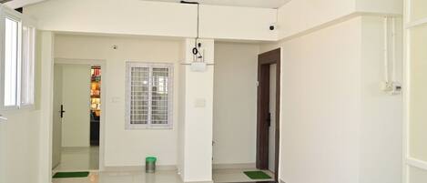 A spacious hallway with a tiled floor, a window with a metal grill, and a door leading to another room.