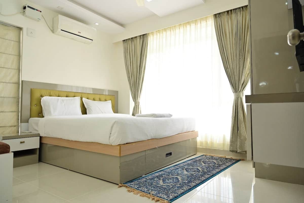 A modern hotel room with a bed, bedside tables, an air conditioning unit, a refrigerator, and a large window with curtains.