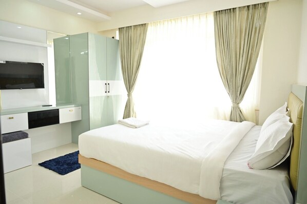 A modern hotel room with a large bed, a flat-screen TV mounted on the wall, a wardrobe, and a bathroom area. - Sai Service Apatment (Bengaluru)