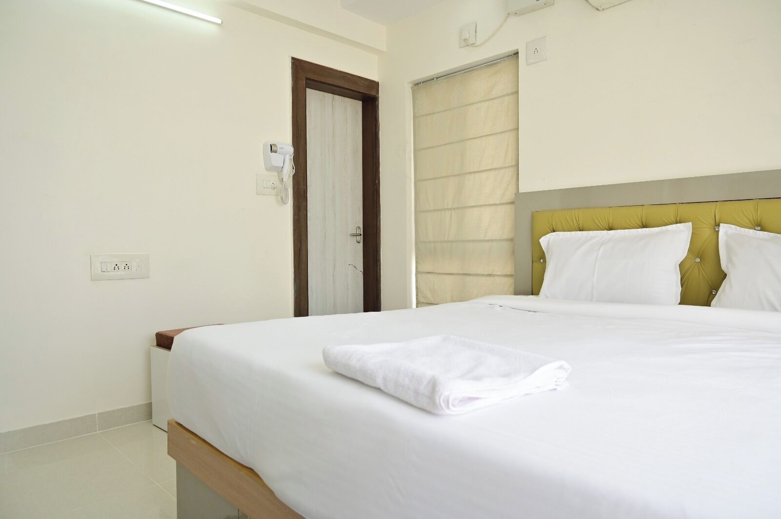 Una habitación de hotel con cama, una mesita de noche de madera, una puerta y una ventana con cortinas.