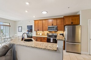 A modern kitchen with wooden cabinets, a stainless steel refrigerator, and a granite countertop. - Bushwood at Delton Grand (Wisconsin Dells)