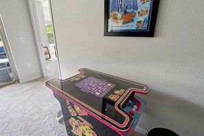 A retro arcade machine with a maze game, a framed poster of a waterpark, and a door leading outside.