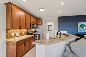 A modern kitchen with wooden cabinets, a granite countertop, a built-in microwave, and a stainless steel refrigerator.