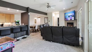 A modern living room with a black leather sofa, a flat-screen TV mounted on the wall, and a kitchen area with bar stools. - Bushwood at Delton Grand (Wisconsin Dells)
