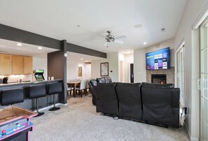 A modern living room with a black leather sofa, a flat-screen TV mounted on the wall, and a kitchen area with bar stools. - Bushwood at Delton Grand (Wisconsin Dells)
