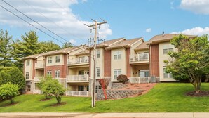 A multi-story apartment building with balconies, a stone retaining wall, and a well-maintained lawn. - Bushwood at Delton Grand (Wisconsin Dells)