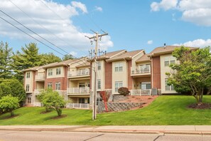 A multi-story apartment building with balconies, a stone retaining wall, and a well-maintained lawn.