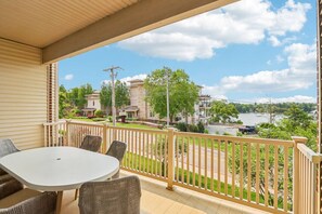 A balcony with a table and chairs, overlooking a lake with buildings and trees.