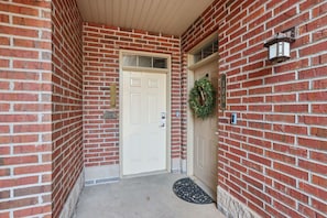 A brick building with a white door, a number plaque, a wreath, and a wall-mounted light fixture.